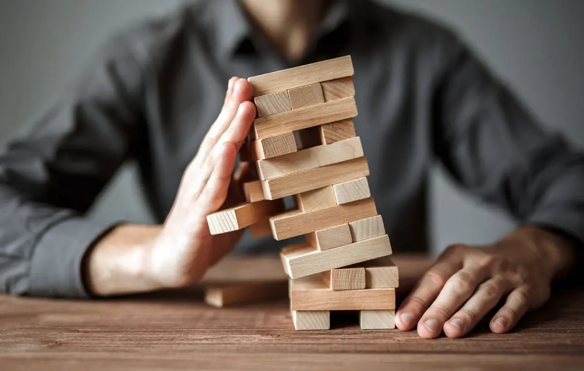 hombre jugando a la Jenga intentando sujetar la torre que se está cayendo
